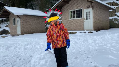 雪玉に手をかける子どもとバンガローの写真
